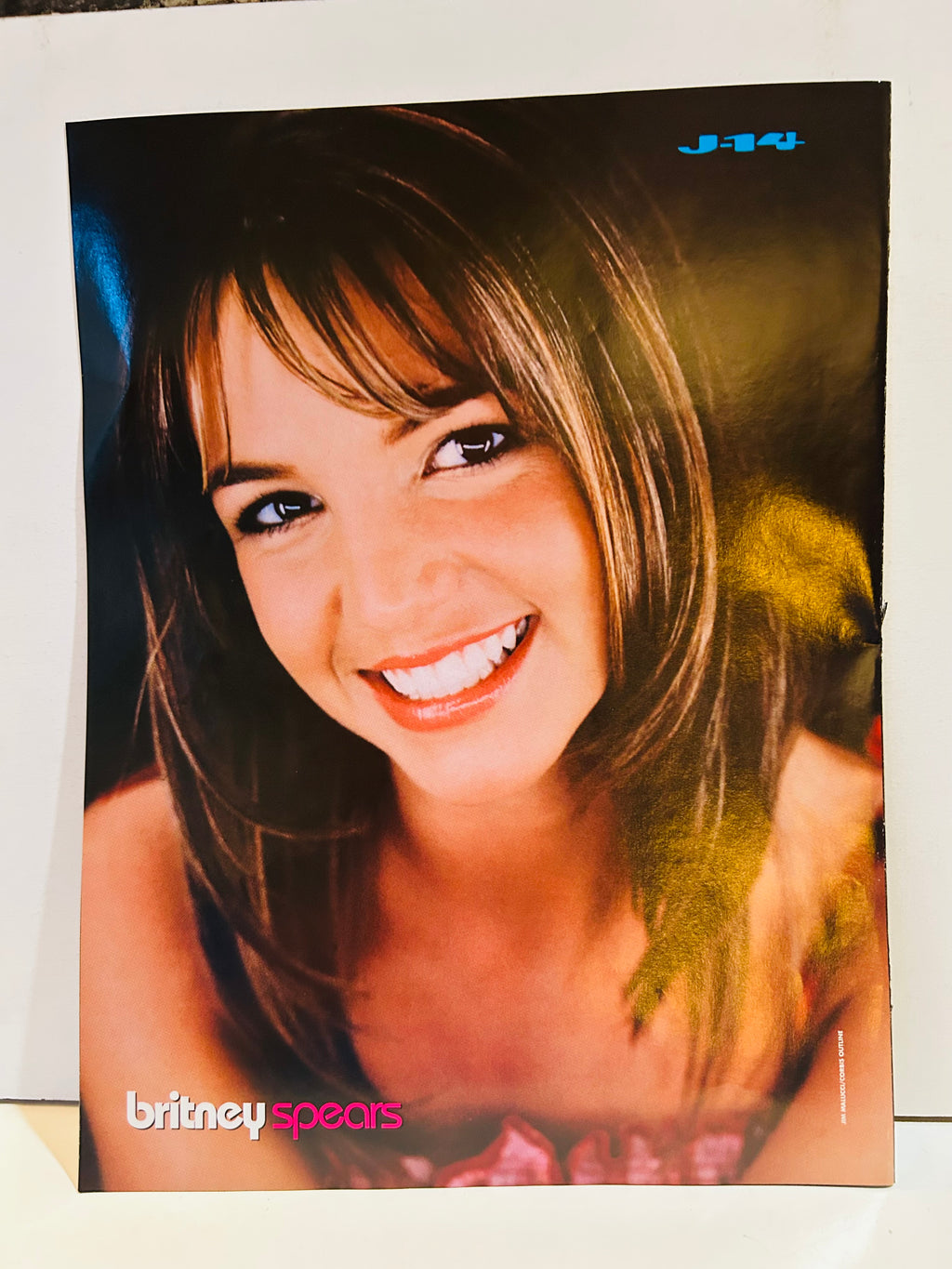 J-14 magazine double-sided poster side B featuring Britney Spears glamour close-up portrait with side-swept bangs smiling warmly wearing pink top, britney spears in pink and white font bottom left, J-14 logo top right