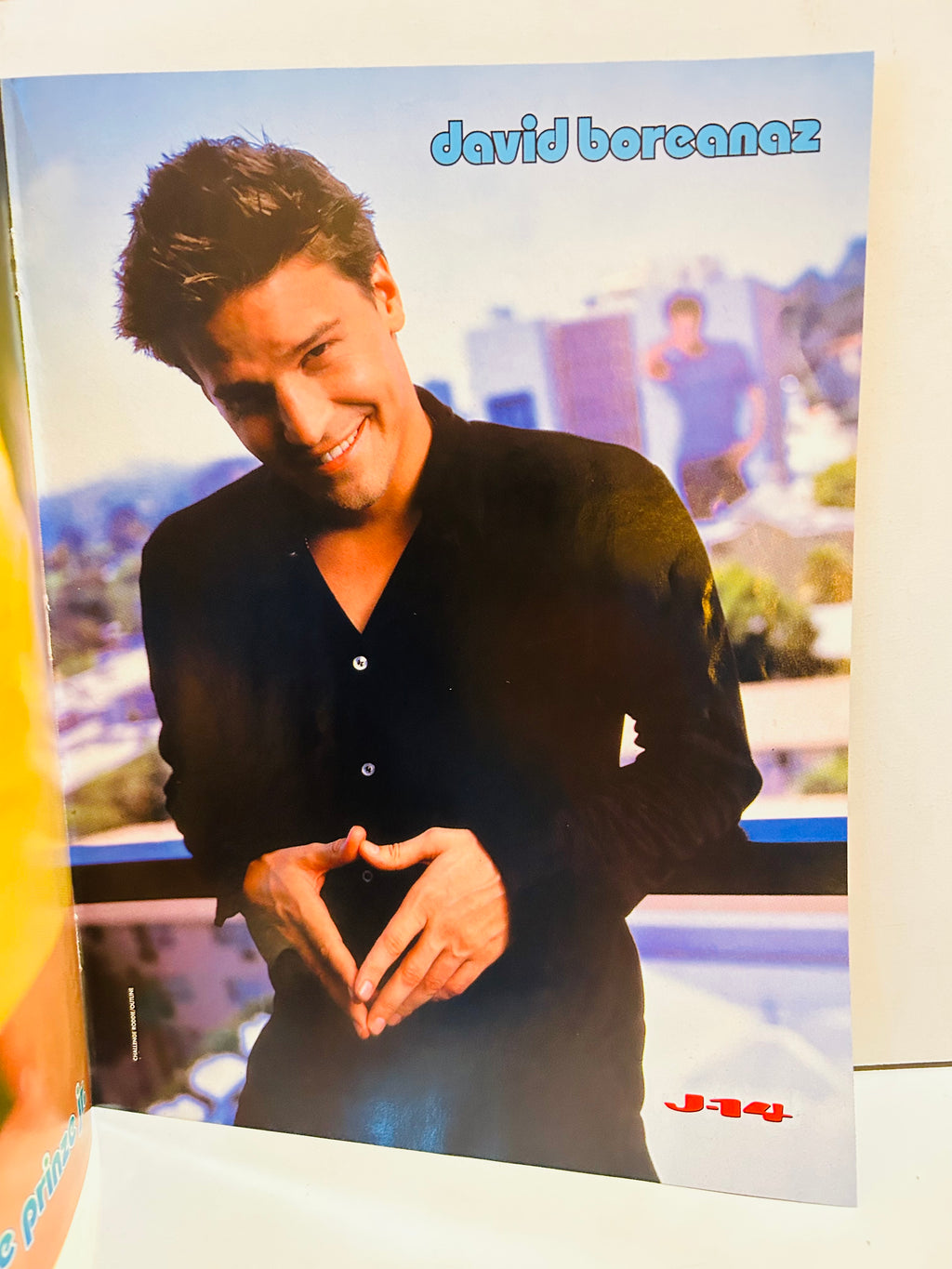 J-14 magazine double-sided poster side A featuring David Boreanaz in black button-down shirt on rooftop making heart shape with hands smiling with city skyline background, david boreanaz in blue bubble font top right, J-14 logo bottom right