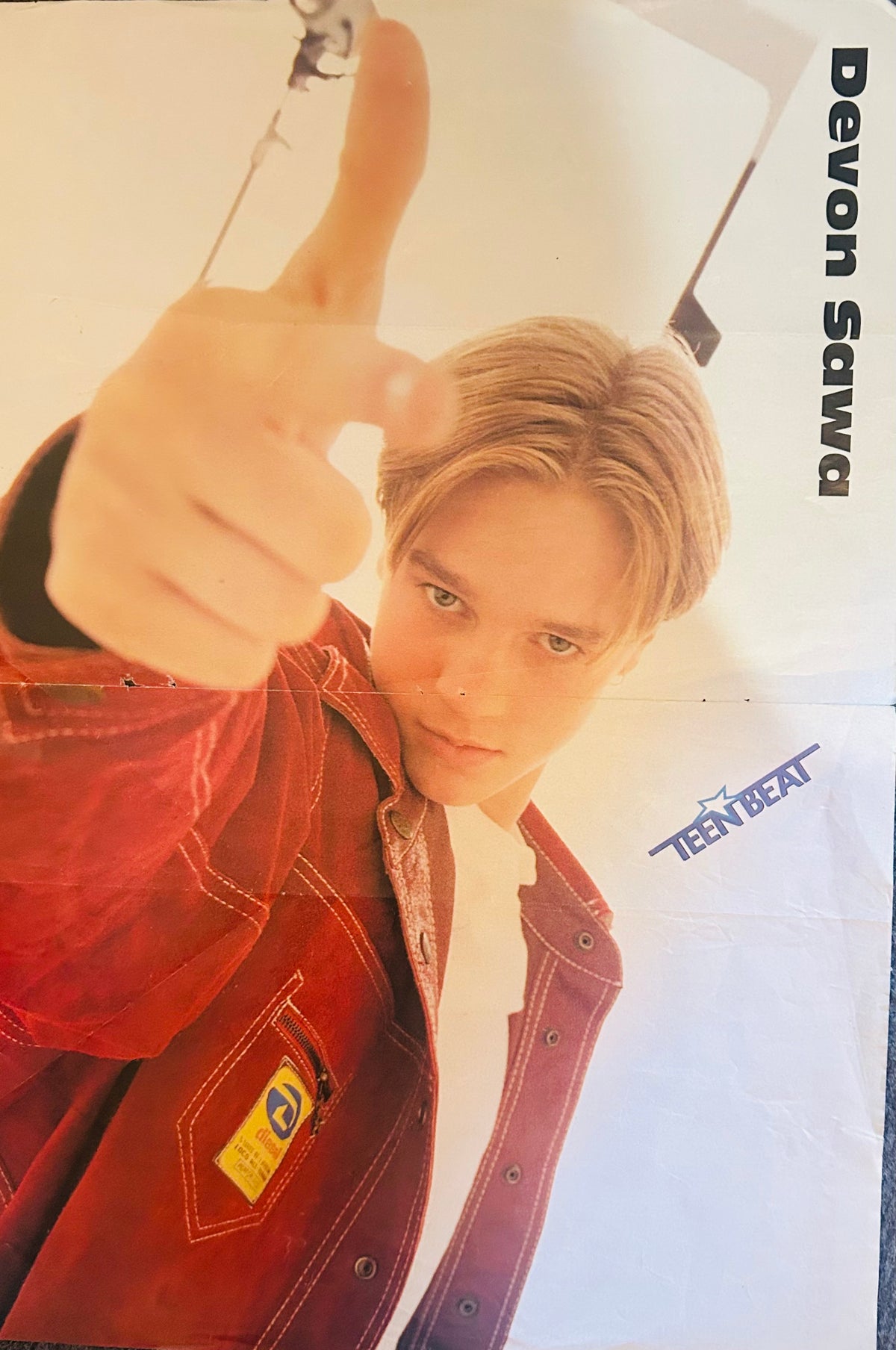 Teen Beat magazine double-sided poster side B featuring Devon Sawa leaning toward camera pointing at viewer wearing red denim jacket with yellow patch against bright white studio background, Devon Sawa in black vertical font right side, Teen Beat logo bottom right