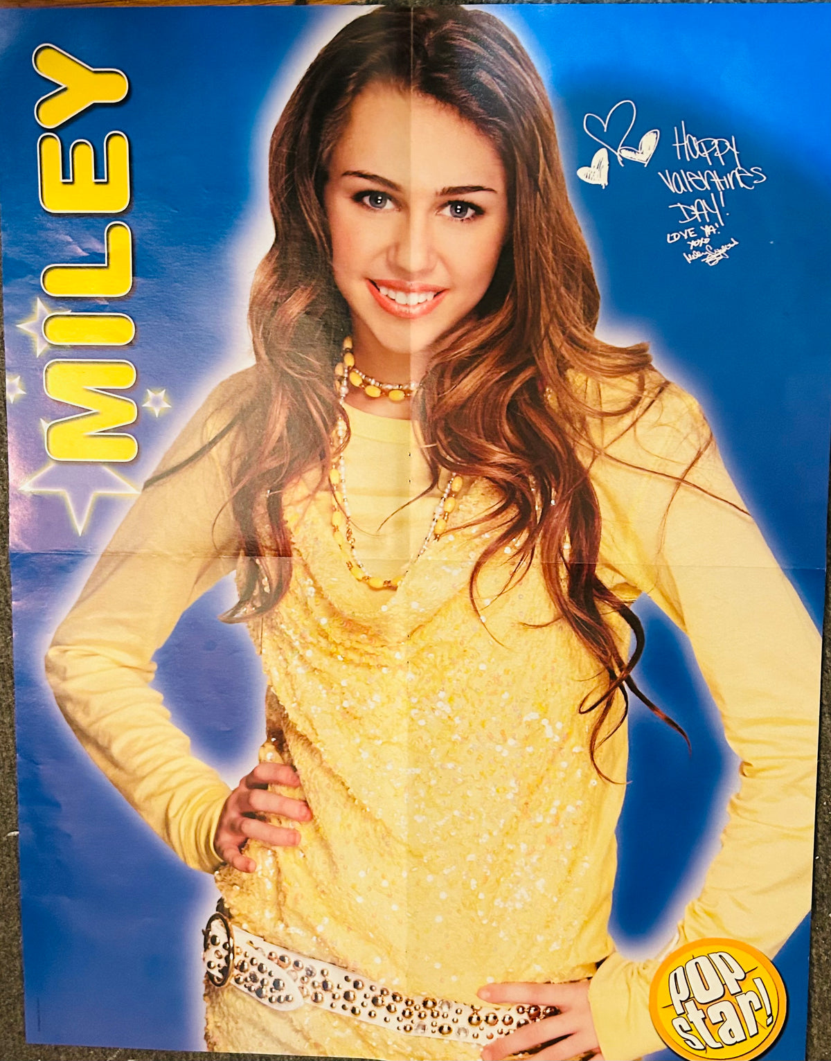 Pop Star! magazine double-sided poster side A featuring Miley Cyrus in yellow sparkly top with layered necklaces against blue starburst background with MILEY in bold yellow text and handwritten Happy Valentine's Day Love Ya xoxo inscription top right