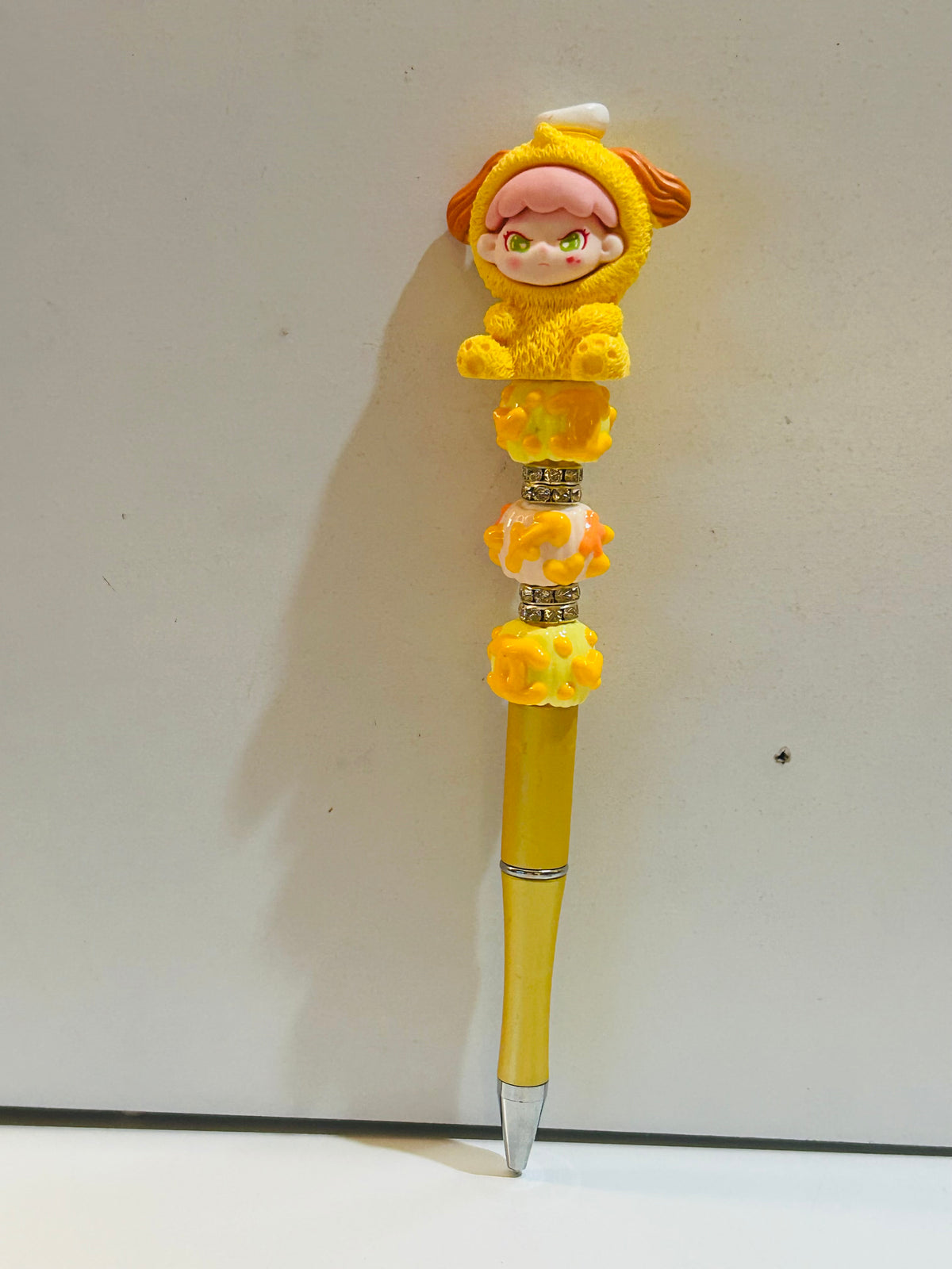 Yellow kawaii beaded ballpoint pen with chibi lion costume character topper, resin beads, and gold-tone spacer rings