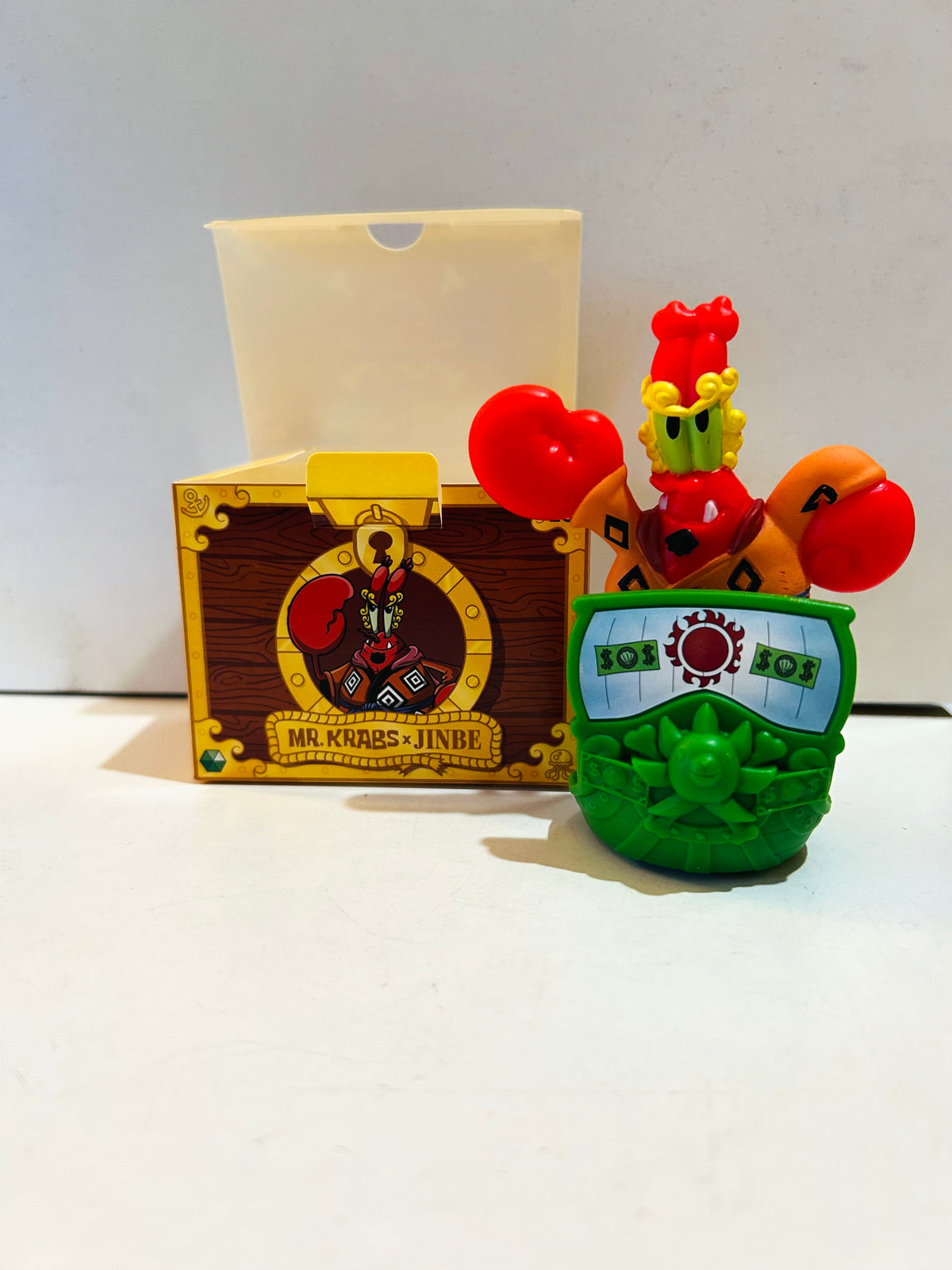 Mr. Krabs x Jinbe collectible figure on green base beside its matching box