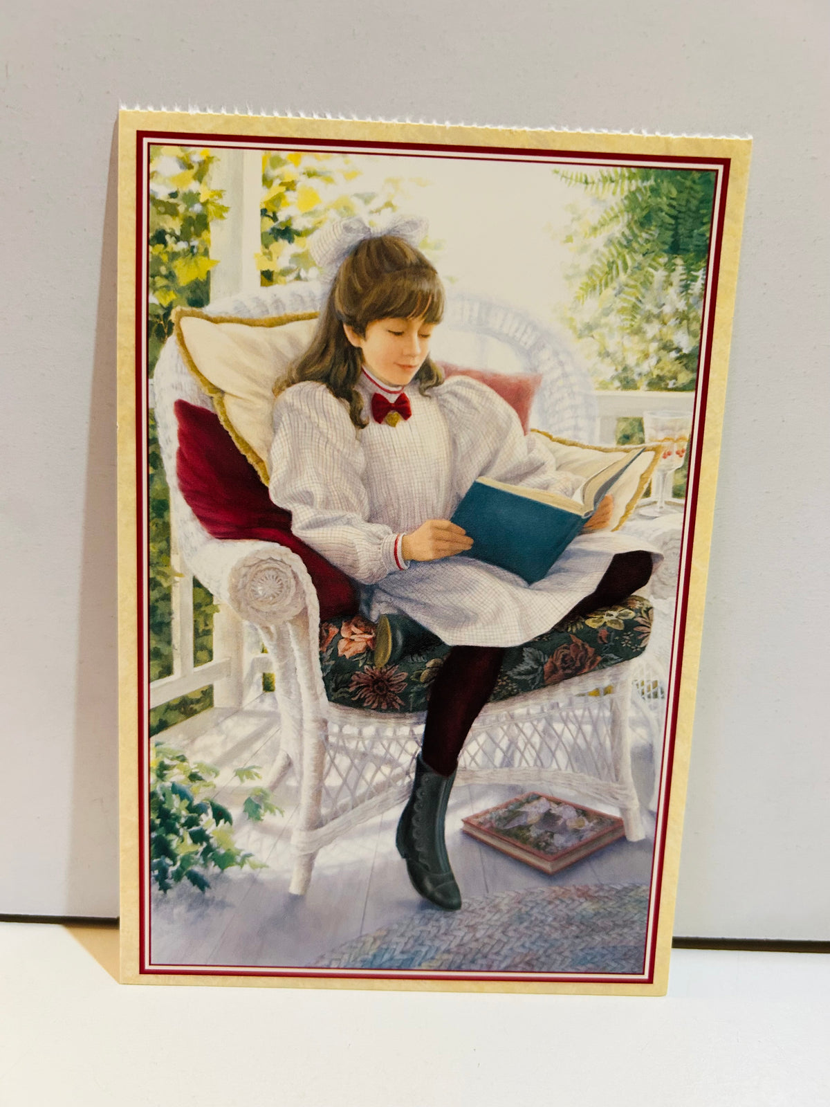 1996 American Girl Samantha collectible postcard featuring painted illustration of Samantha in white puffed-sleeve dress with red bow sitting on white wicker settee on sunlit porch reading a blue book