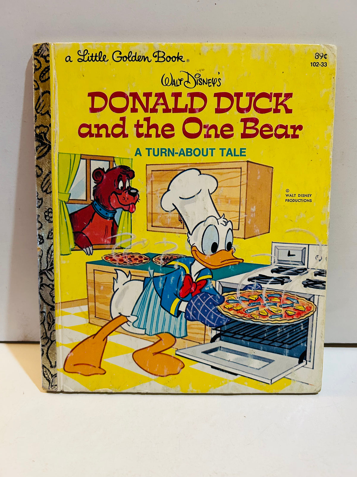 Walt Disney's Donald Duck and the One Bear A Turn-About Tale Little Golden Book 1978 cover featuring Donald Duck in chef hat baking pizza at stove with a bear peering through kitchen window, yellow background, item 102-33