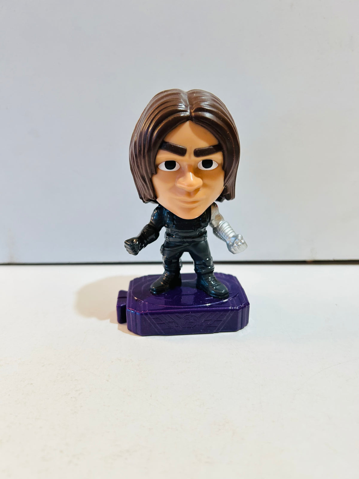 Marvel Winter Soldier Bucky Barnes chibi style mini collectible figure approximately 2 inches tall on purple display base wearing black tactical outfit with silver vibranium left arm detail and brown shoulder-length hair