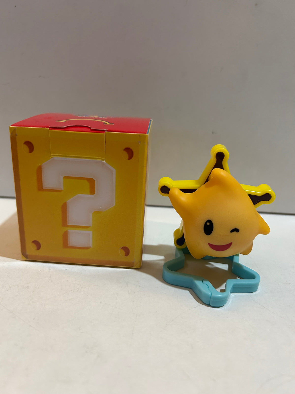 Winking yellow star figure on a blue star-shaped base beside a yellow question-mark block box