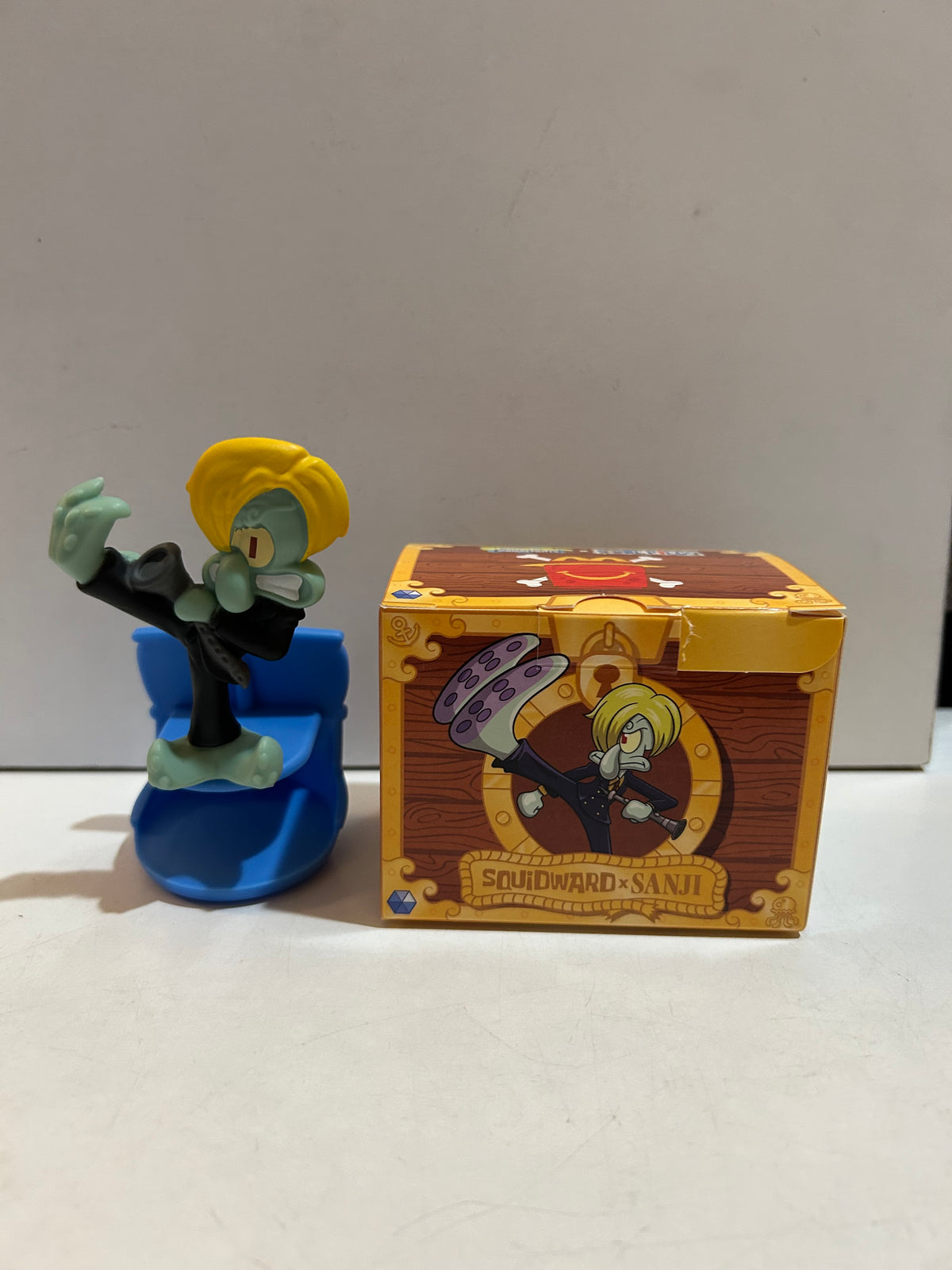 Squidward dressed as Sanji with yellow hair and black suit on a blue base beside its Squidward x Sanji box
