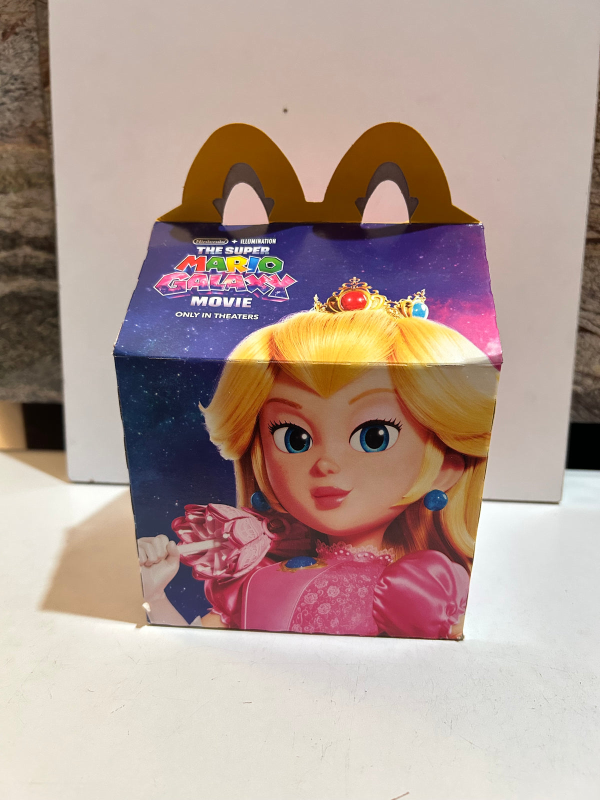 Super Mario Galaxy Movie Happy Meal box featuring Princess Peach against a starry background with yellow arch handles