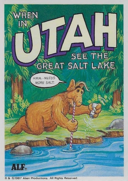 U.S. of ALF Utah sticker featuring ALF crouched at Great Salt Lake shoreline sipping through straw while shaking salt shaker into it saying hmm needs more salt