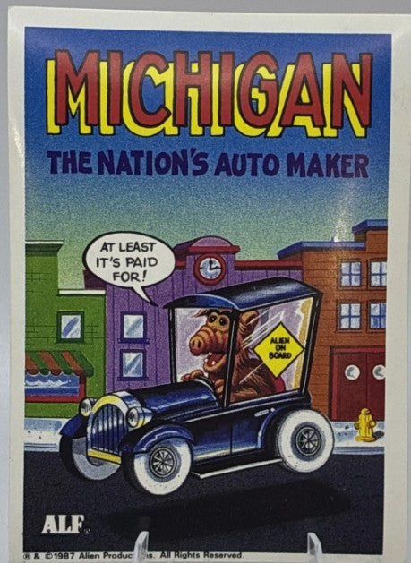 U.S. of ALF Michigan sticker featuring ALF driving a vintage dark blue Model T car with Alien on Board sign saying at least its paid for